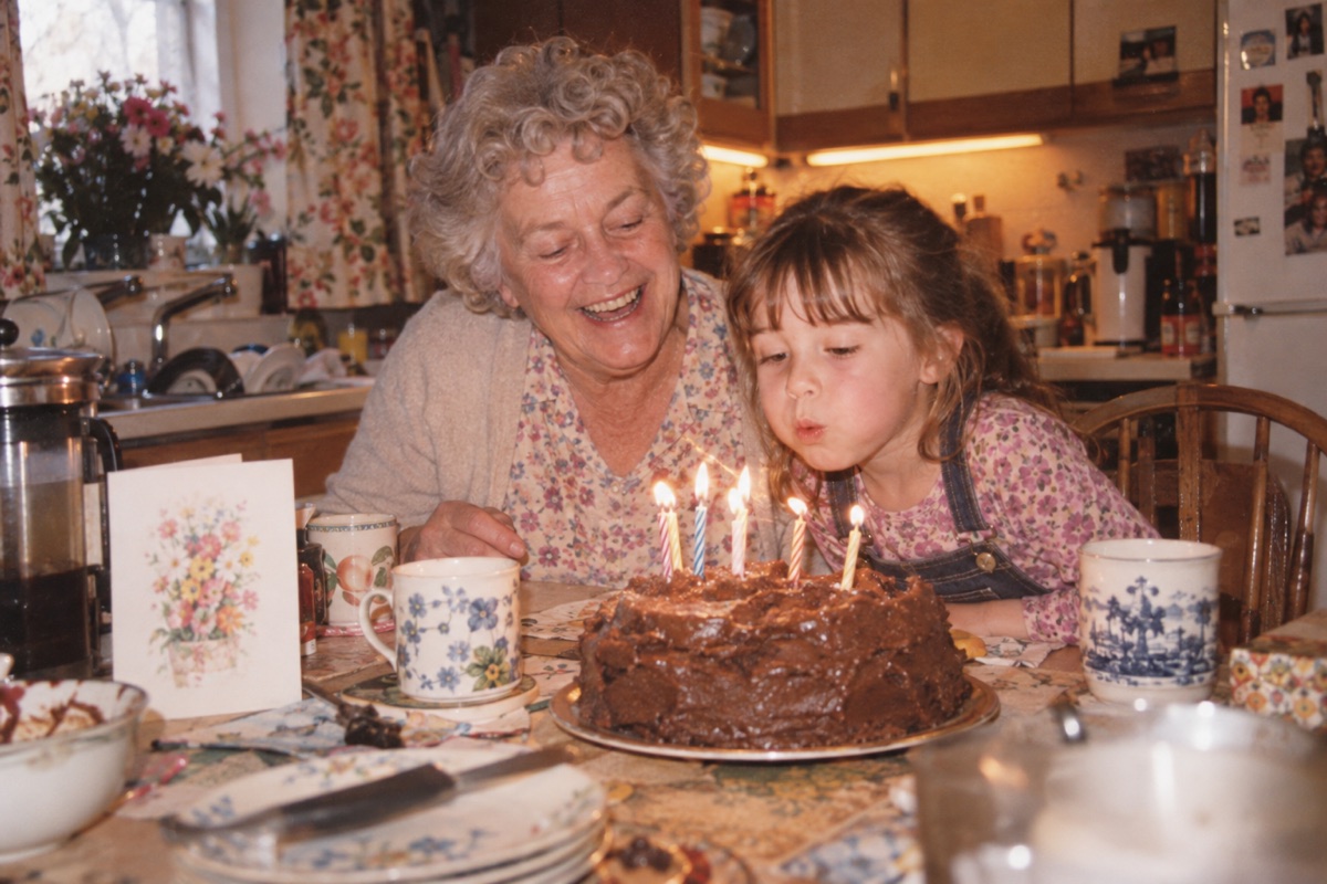 Fictional 2004 snapshot of a grandmother and granddaughter blowing out birthday candles at a kitchen table